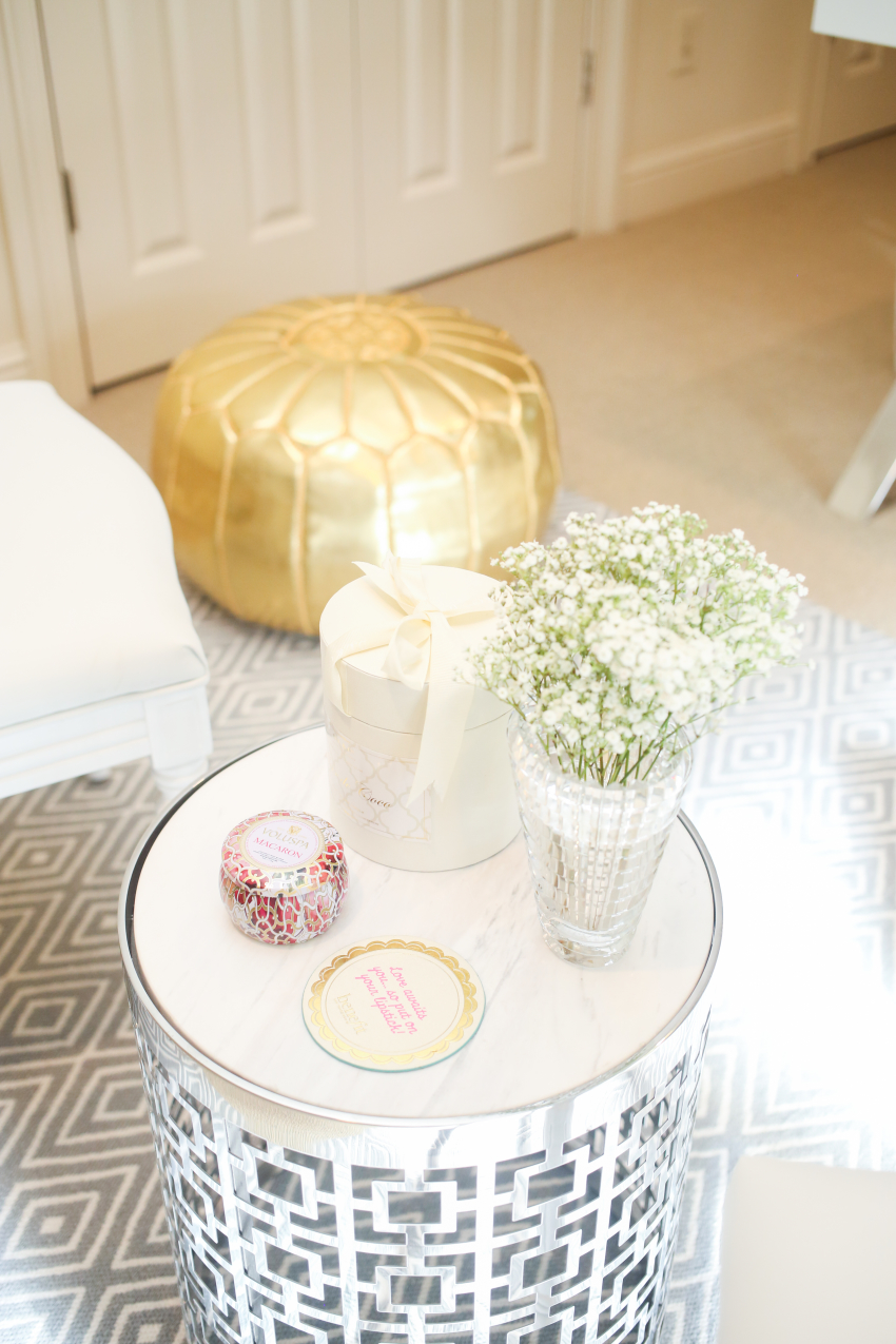 Gold Rachel George Pouf and Silver patterned Jonathan Adler marble side table with Voluspa and D.L. & Co. Candle with Babys Breath on a Grey and White Pattern Rug on Fashionable Hostess