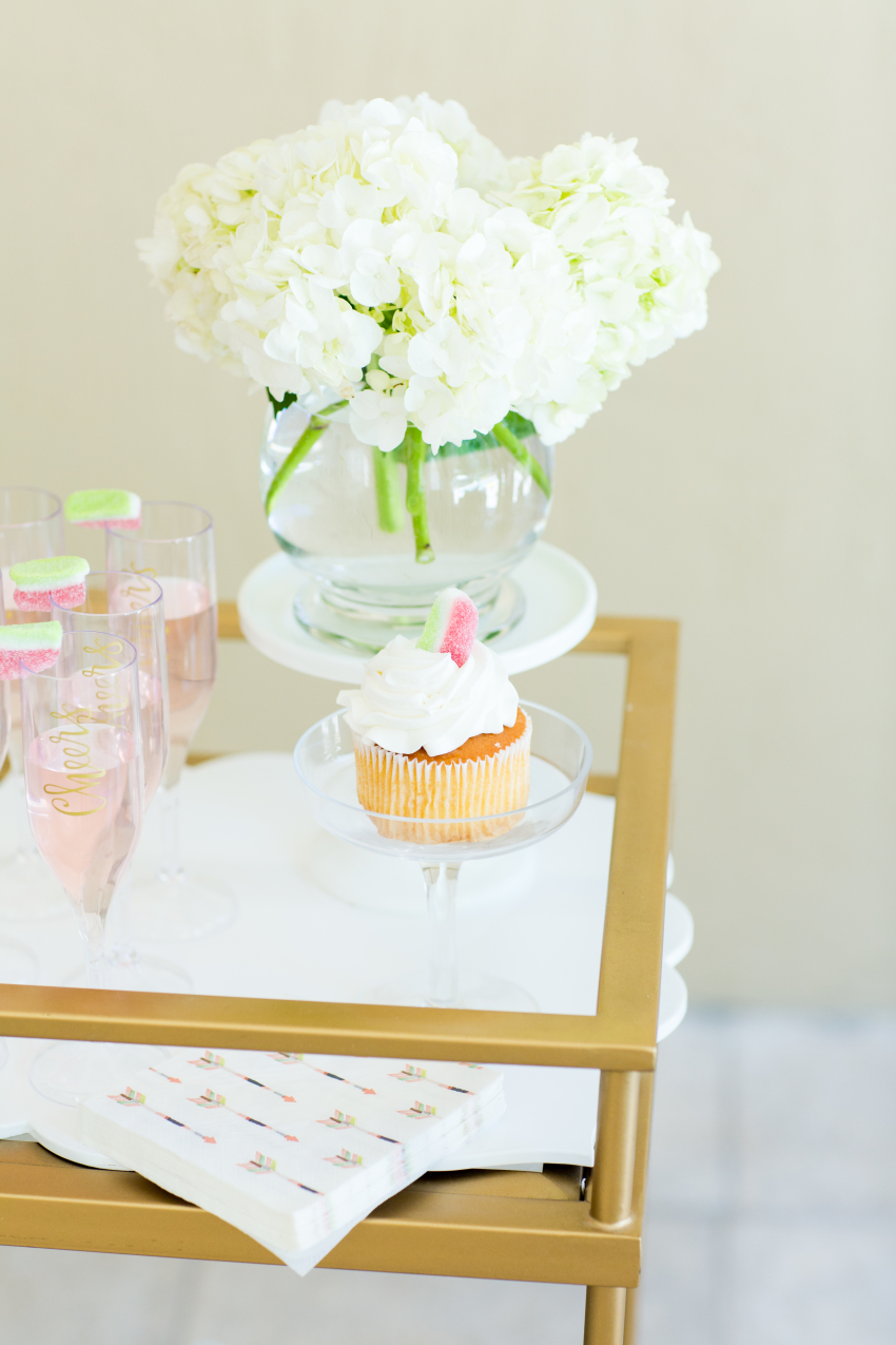 Cupcakes and decorative champagne glasses topped with watermelon candy on gold bar cart for Spring on FashionableHostess.com